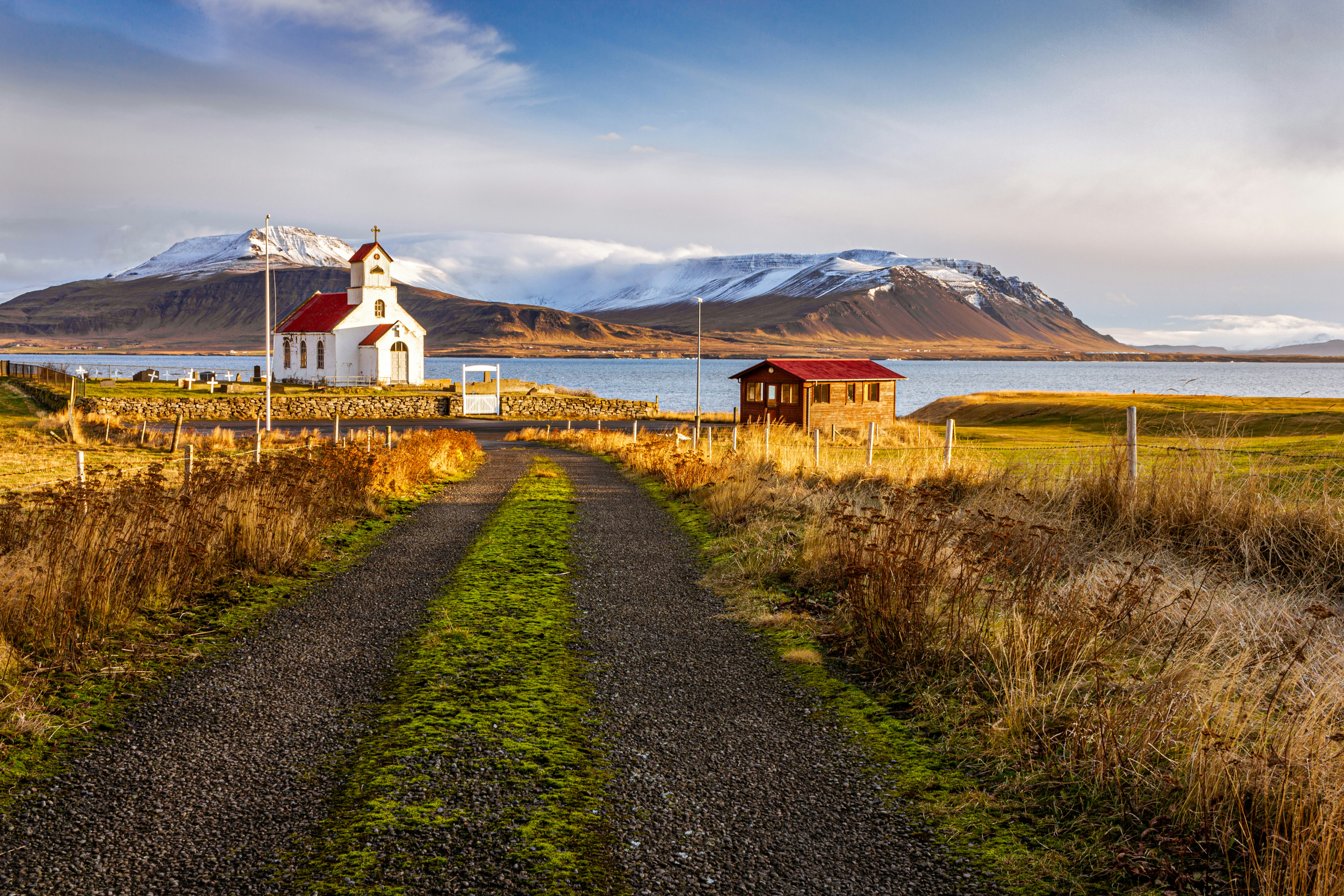 Trail that leads you to Church and house within Akranes, with a mountain and lake behind them.